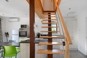 Eine moderne Küche mit einer zentralen Holztreppe, Edelstahlgeräten und einer hellen, freundlichen Atmosphäre.