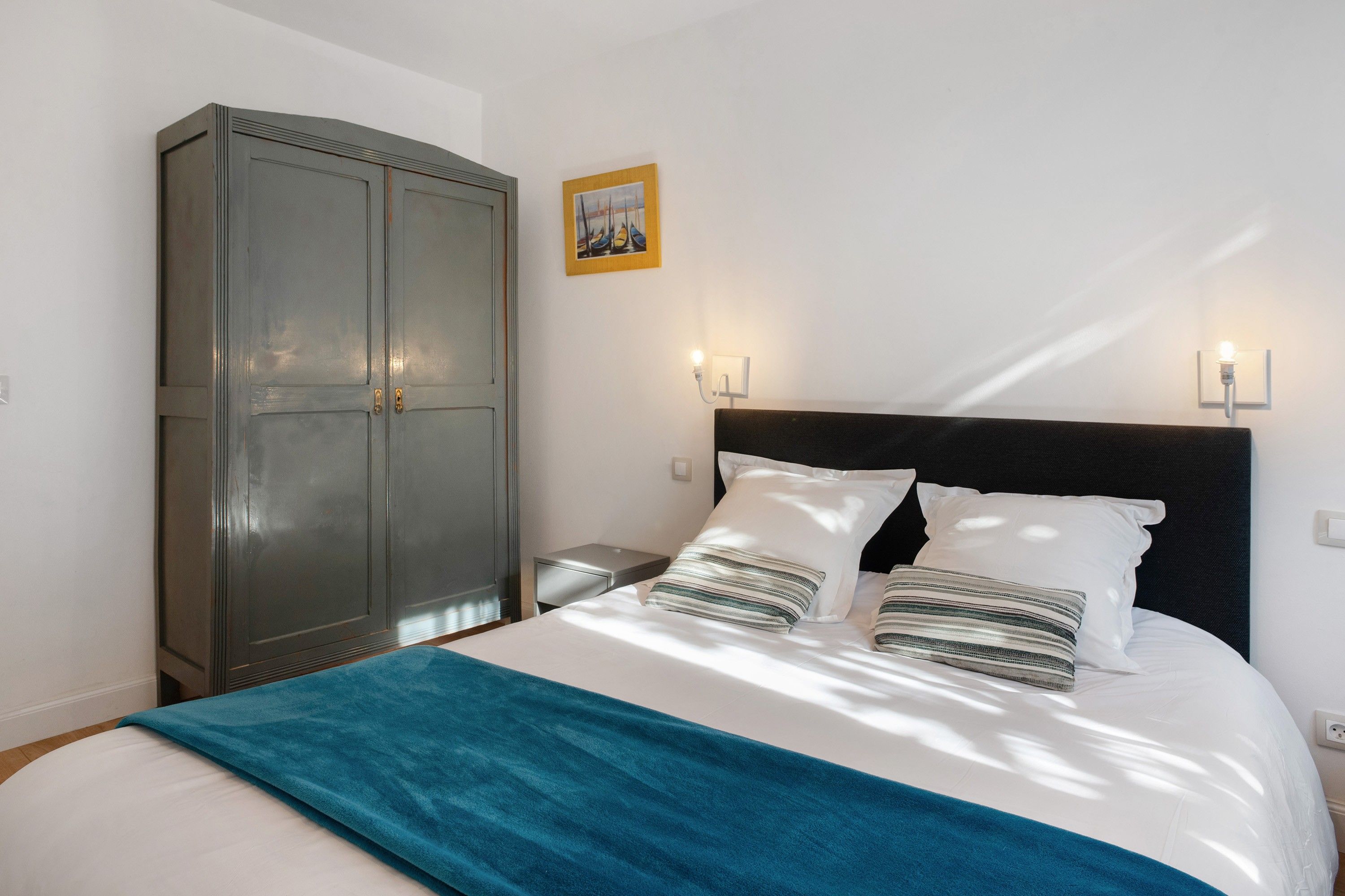 Un dormitorio con cama, armario y dos luces fijadas a la pared.