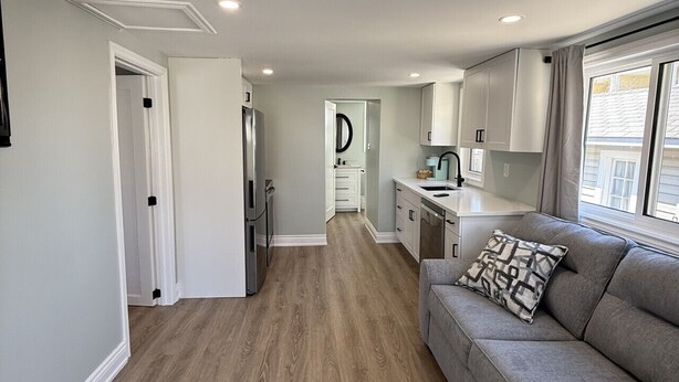 A modern kitchen with white cabinets, a grey sofa, and a wooden floor. - ORS Beach Corporation | Wasaga Beach Rental (Wasaga Beach)