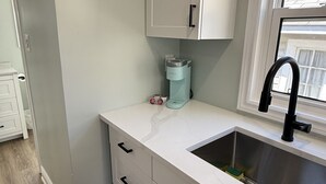 A kitchen with a white countertop, a stainless steel sink, and a window with a view of the outside. - ORS Beach Corporation | Wasaga Beach Rental (Wasaga Beach)