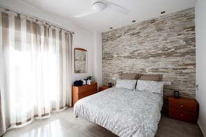 Een slaapkamer met een bed, nachtkastje, dressoir, spiegel en een wand met mozaïekpatroon.