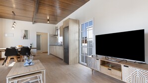 Una sala de estar moderna con un televisor de pantalla plana grande, piso de madera y una zona de comedor con una mesa y sillas.