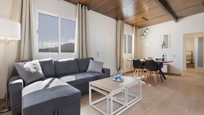 Una sala de estar moderna con un sofá modular, un comedor con mesa y sillas, y un amplio ventanal con cortinas.