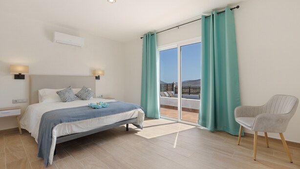 Un dormitorio con cama, una silla, un balcón con cortinas y vistas al exterior.