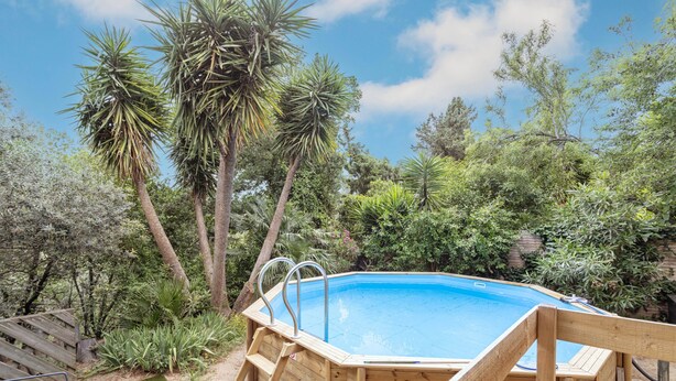 A wooden hot tub surrounded by lush greenery and trees.