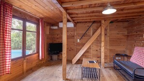 A wooden cabin interior with a bed, a table, a TV, and a staircase.