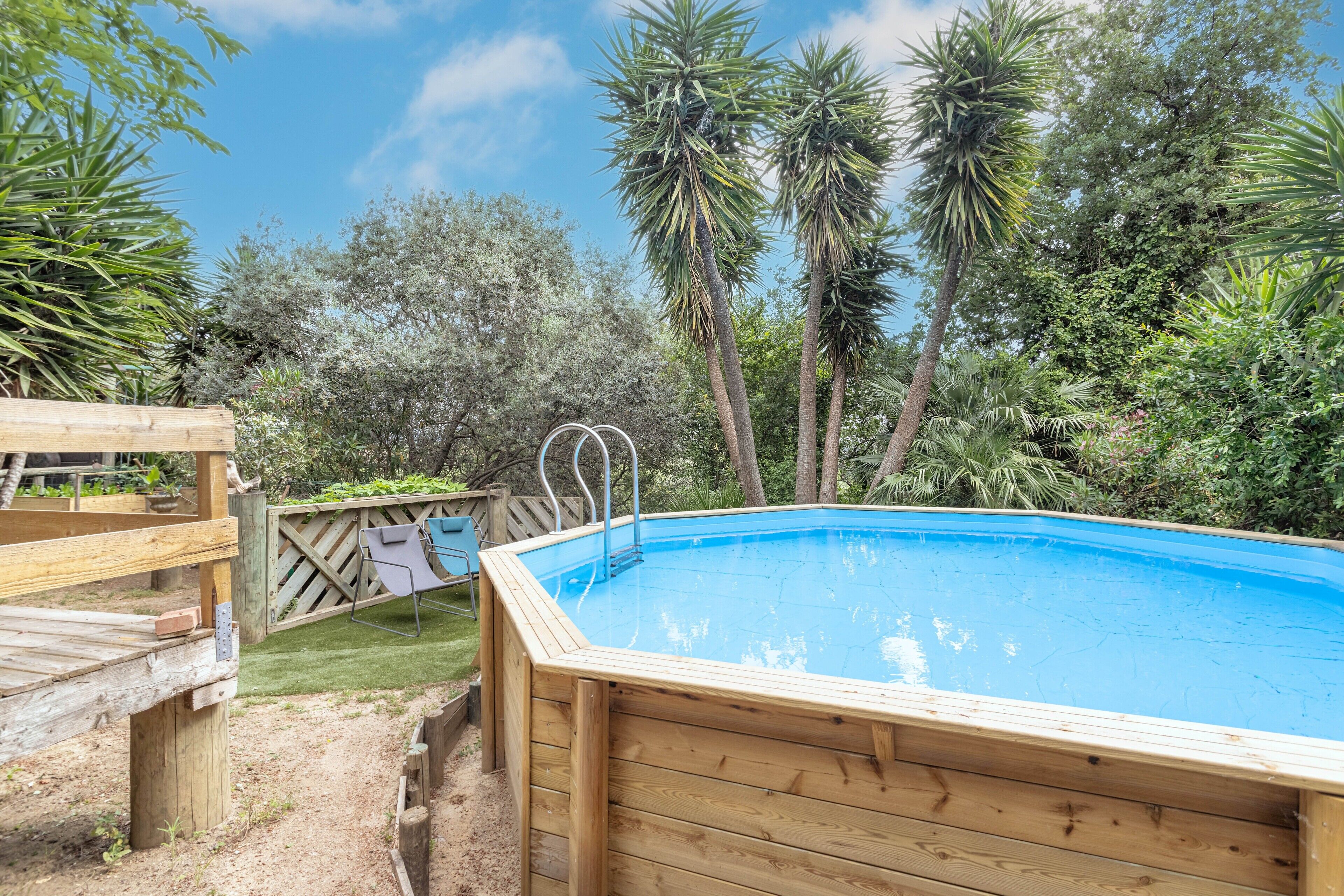 Una piscina in legno con una scala, immersa nel verde e circondata da alberi.