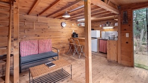 A wooden cabin interior with a sofa, chairs, a dining table, a kitchen area, and a large window.