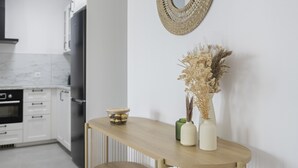 Een moderne keuken met witte kasten, een houten tafel met twee vazen en een geweven spiegel aan de muur.