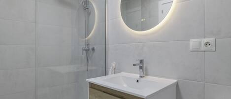 Un baño moderno con ducha, lavamanos, espejo e inodoro.