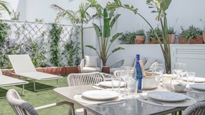 Een buitenterras met tafels gedekt voor een maaltijd, omringd door potplanten en stoelen.