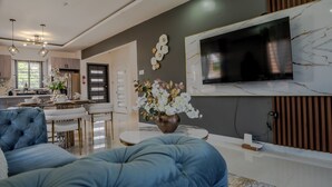 A modern living room with a large flat-screen TV, a blue sofa, and a dining area with a white table and chairs. - Rooftop Villa partial Sea view/ Mountain views (Ocho Rios)