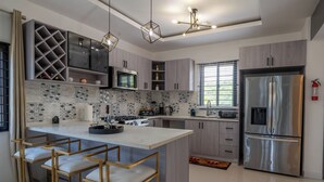 A modern kitchen with a central island, bar stools, a stainless steel refrigerator, and a patterned backsplash. - Rooftop Villa partial Sea view/ Mountain views (Ocho Rios)