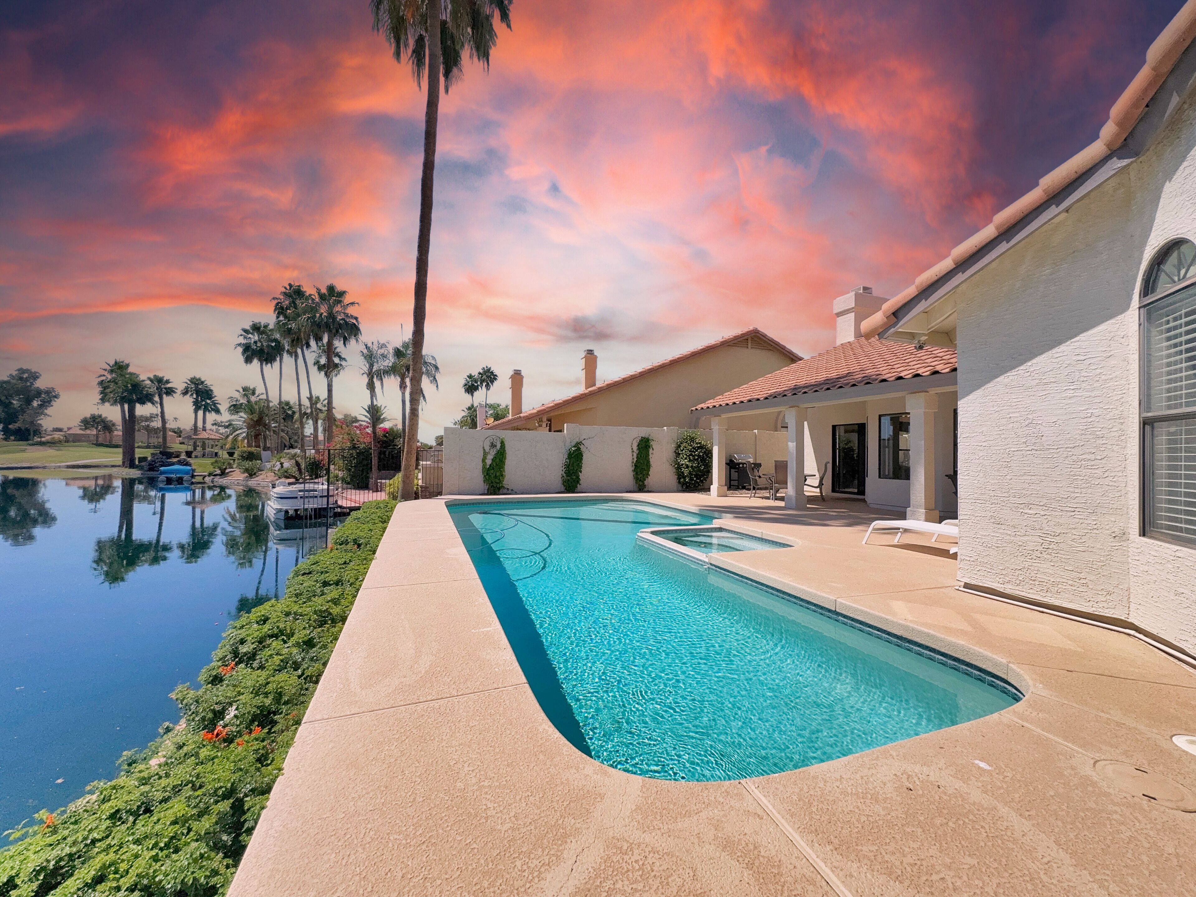 Ein Pool mit geschwungener Kante, umgeben von einer Terrassenfläche mit Stühlen und einer überdachten Sitzgelegenheit.