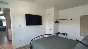 Ein Schlafzimmer mit einem Bett, einem an der Wand montierten Fernseher, einer Tür und einem Flur, der in einen weiteren Raum führt.