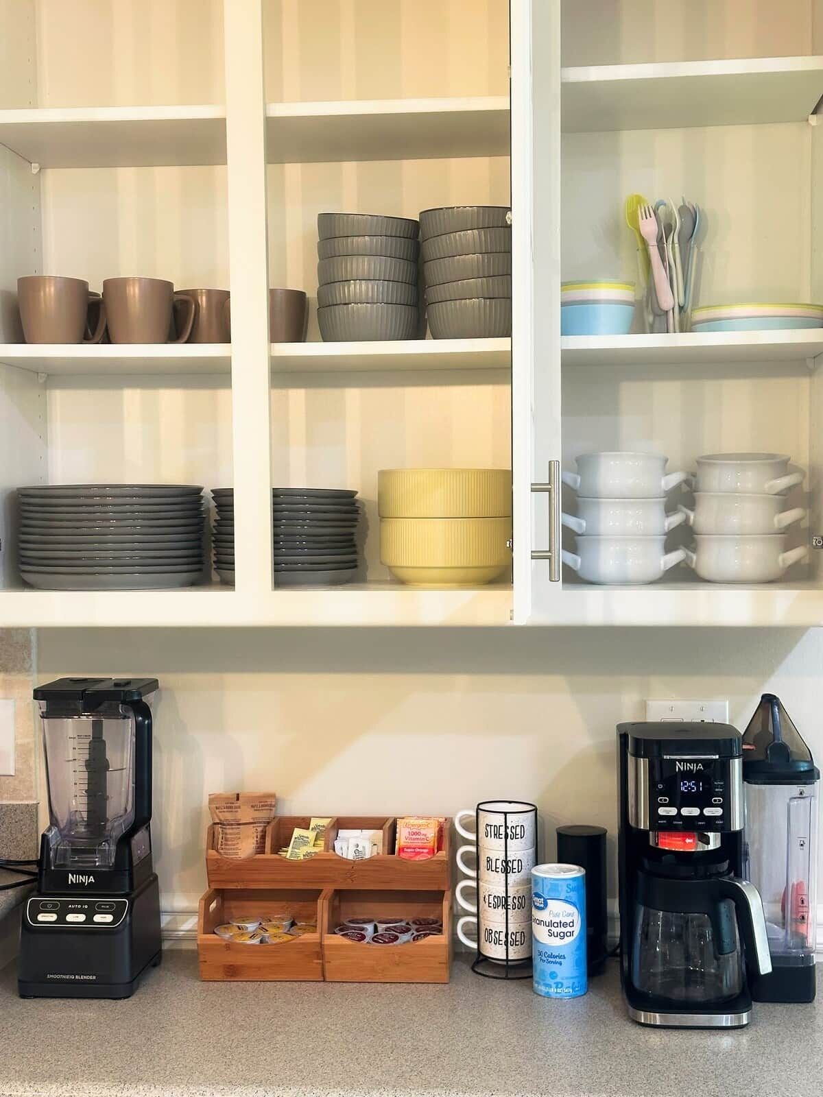 A kitchen with white cabinets, a coffee maker, a blender, and various kitchenware.