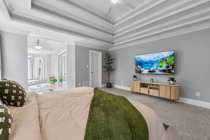 Un salon moderne avec un grand téléviseur à écran plat, un meuble TV en bois et un plaid vert sur le lit.