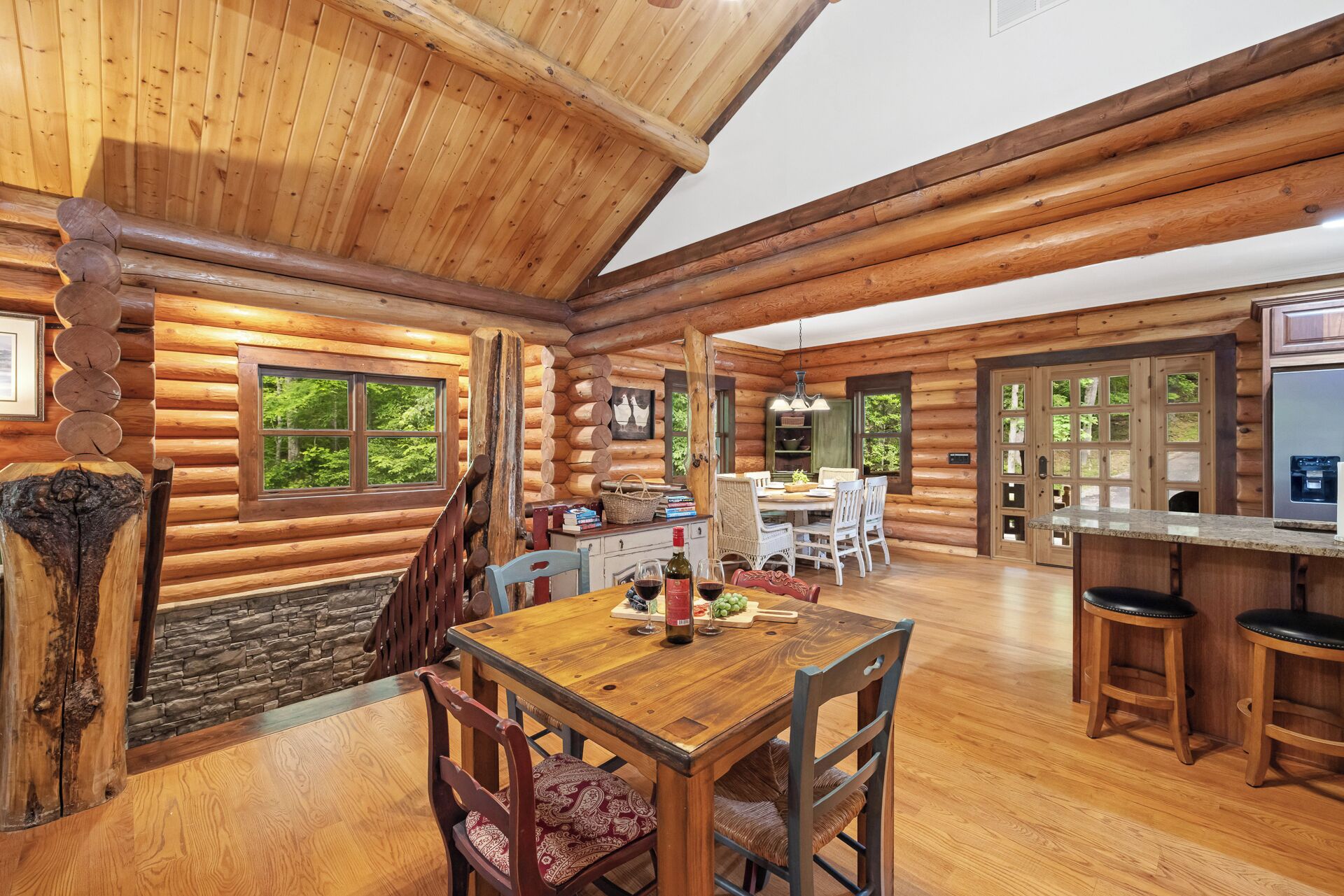 A log cabin interior with a dining area, kitchen, and stone fireplace.