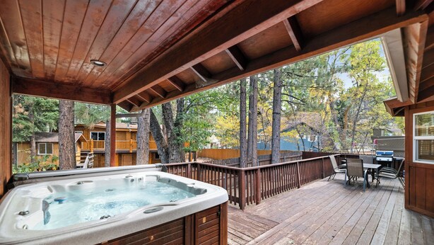 Une terrasse en bois avec un jacuzzi, du mobilier d’extérieur et une vue sur les arbres et une maison.