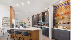 Una cocina moderna con una isla central, taburetes de bar, un botellero y un ventanal grande.