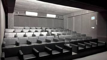 Un cine moderno con hileras de asientos de cuero negro, una pantalla grande y un diseño minimalista.