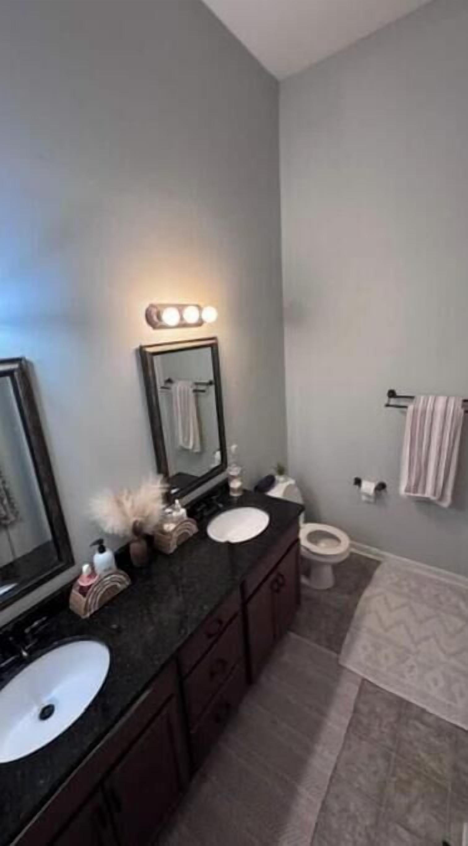 A bathroom with a dark countertop, a mirror, a towel rack, and a toilet.