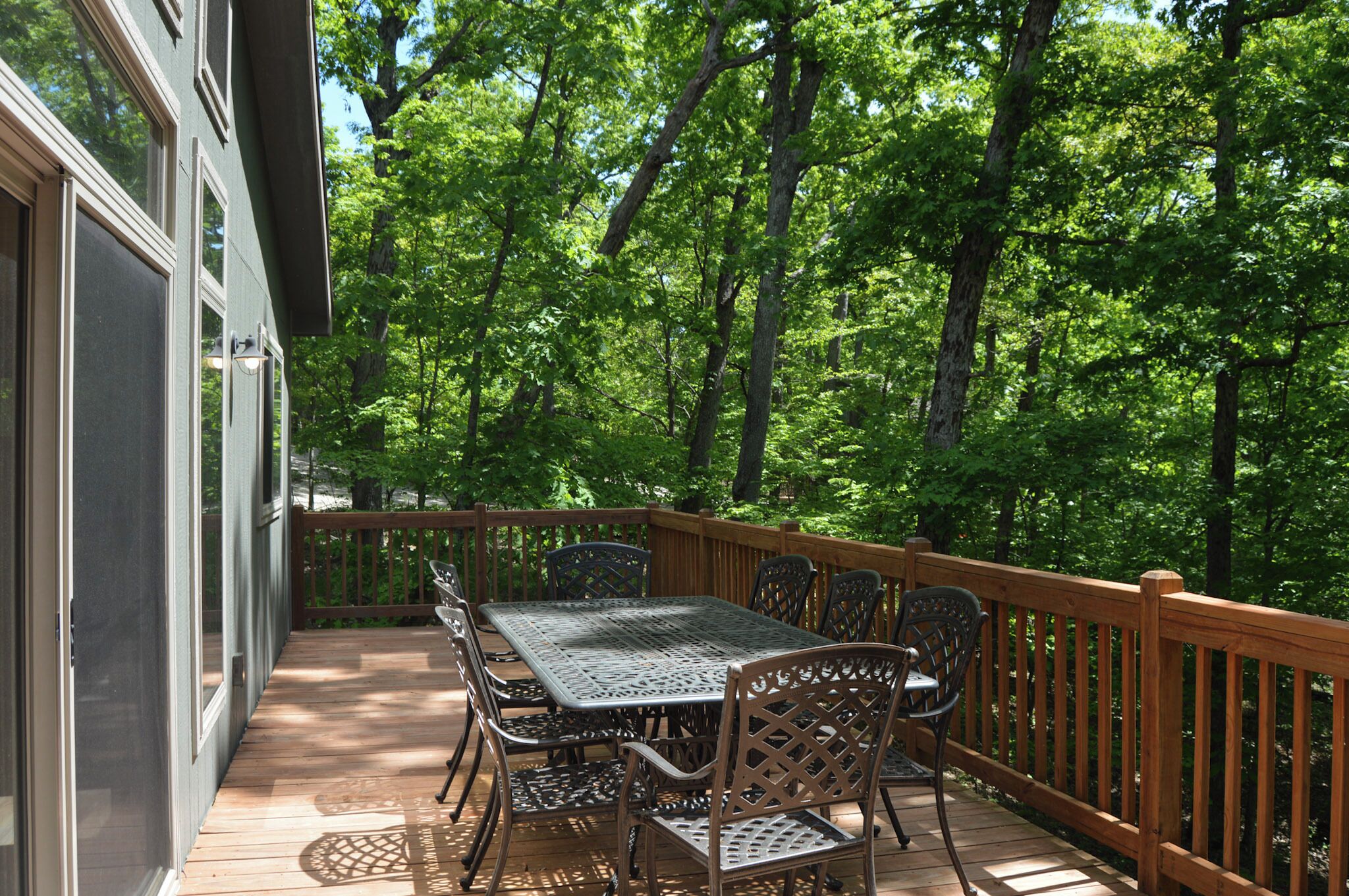 A deck with a table and chairs, surrounded by a wooden railing, overlooking a forested area.
