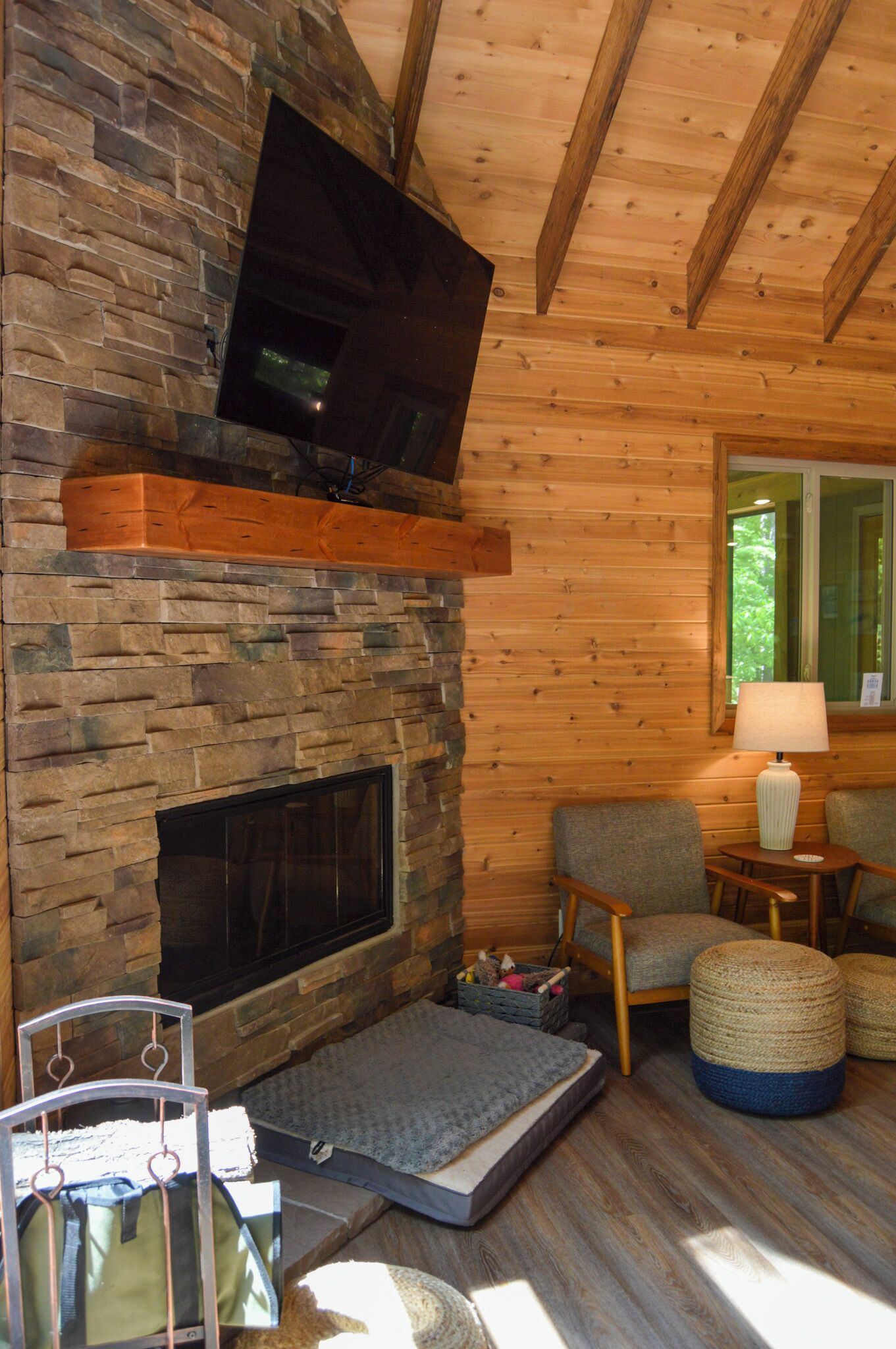 A cozy room with a stone fireplace, a flat-screen TV mounted above it, and a comfortable seating area with a lamp and ottomans.
