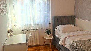 Un dormitorio con cama, escritorio, silla y una mesita con una planta.