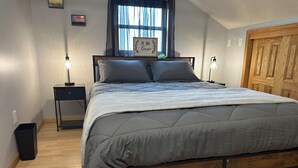 Un dormitorio con una cama, mesitas de noche, un ventanal con cortinas, un armario de madera y un cuadro colgado en la pared.
