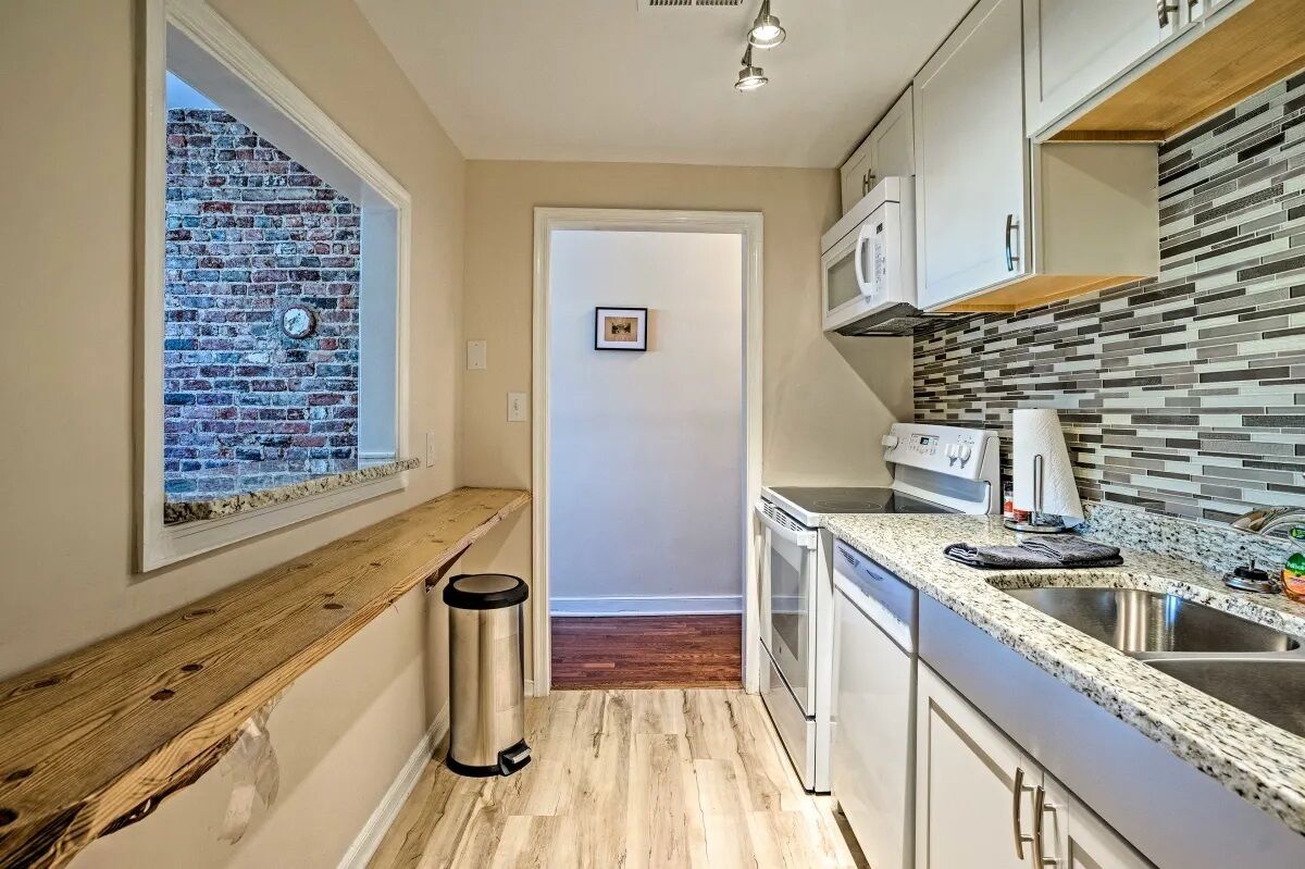 A modern kitchen with a brick wall, wooden bench, stainless steel appliances, and a tiled backsplash.