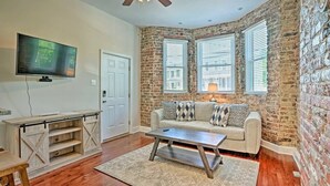 A living room with a brick wall, a sofa, a coffee table, a TV, and a wooden cabinet. - Charming Historic 1-bedroom apartment with WiFi, AC in pleasant Richmond (Richmond)