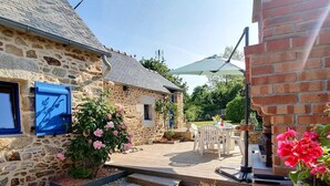 A stone building with a wooden deck, outdoor seating, and a large umbrella. - Ty Luz - CAMLEZ - Gîte (CAMLEZ)