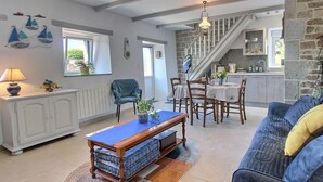 A spacious living area with a dining table, chairs, a sofa, and a staircase leading to a kitchen. - Ty Luz - CAMLEZ - Gîte (CAMLEZ)