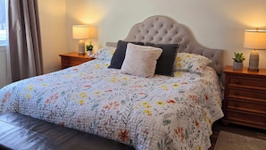 Un lit bien fait, avec une couette à motifs floraux, une tête de lit capitonnée et deux tables de chevet avec des lampes.