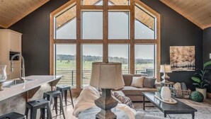 A spacious living area with a large window, a dining area, and a kitchen.