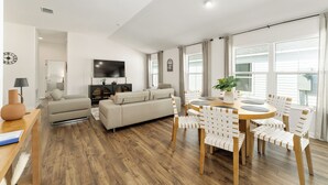 A modern living room with a sofa, a dining table with chairs, a TV, and a wooden floor. - DISCOUNTED 2-bed Patio Villa in Waters Edge, near Eastport. Avail. Nov, Dec, Jan (The villages)