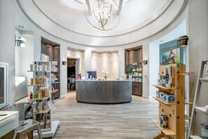 Un interior moderno con una recepción central, estanterías de madera con productos y una araña.