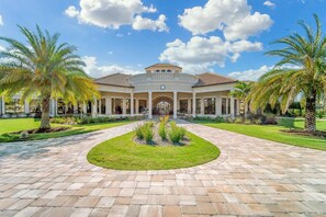 A large, two-story building with a central courtyard, surrounded by palm trees and a well-maintained lawn.