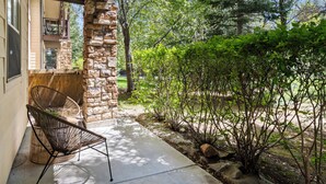 A covered patio with a stone pillar, a wicker chair, and a small garden area with shrubs and a pathway.
