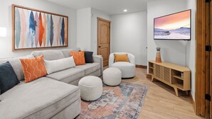 A modern living room with a sectional sofa, ottomans, a flat-screen TV, and a wooden TV stand.
