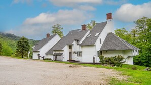 Una hilera de casas blancas con techos grises, un camino de grava y montañas al fondo.