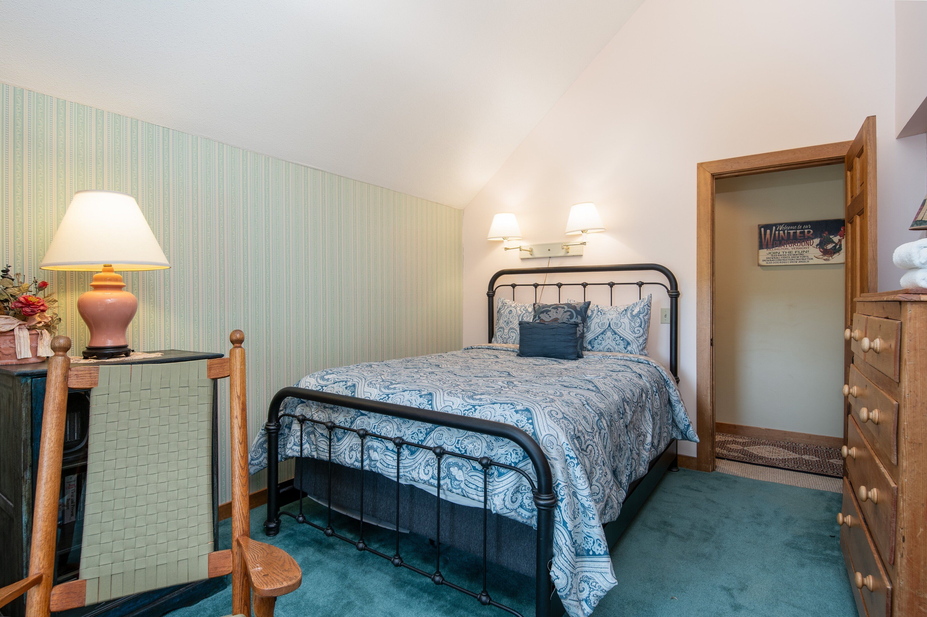 Een slaapkamer met een bed, nachtkastje, lamp en een kast.