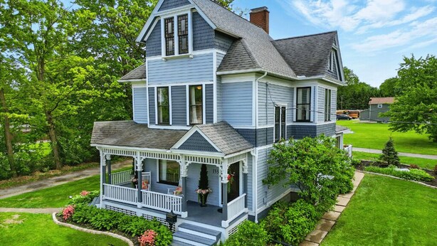 A two-story house with a porch, surrounded by a well-maintained lawn and trees.