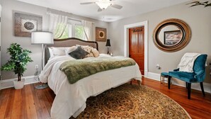 A bedroom with a bed, a ceiling fan, a door, a chair, and a rug.