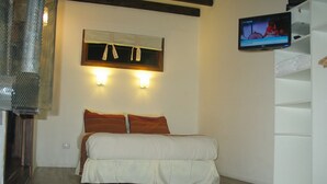 A bedroom with a bed, two wall-mounted lights, a TV on the wall, and a wooden floor. - Fehu Container Lofts (Villa La Angostura)