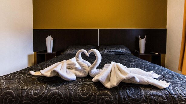 A hotel room with a bed featuring a heart-shaped towel arrangement. - Hotel Santander (Villa Carlos Paz)