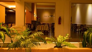 A hotel lobby with a seating area, tables, and chairs. There are potted plants and a fire extinguisher on the wall. - Hotel Santander (Villa Carlos Paz)