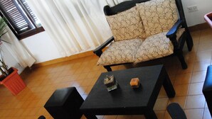 A living room with a sofa, two black tables, and potted plants.
