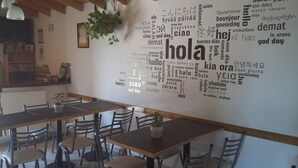 Un comedor con una mesa larga y sillas, una planta colgante y una pared con palabras en varios idiomas.